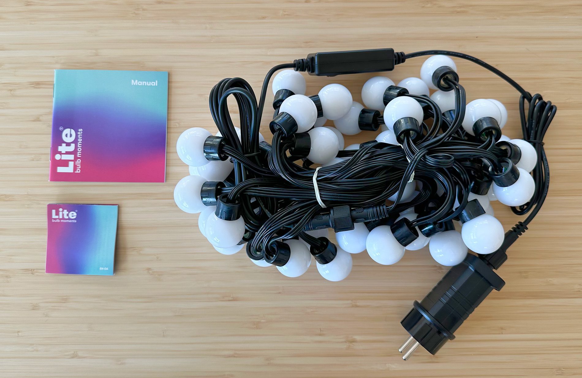 Hier sieht man den Lieferumfang der Smart String Lights LED-Lichterkette: Die Lichterkette mit der Bedienbox und dem Steckernetzteil, sowie der Anleitung und einem Hinweis-Faltblatt.