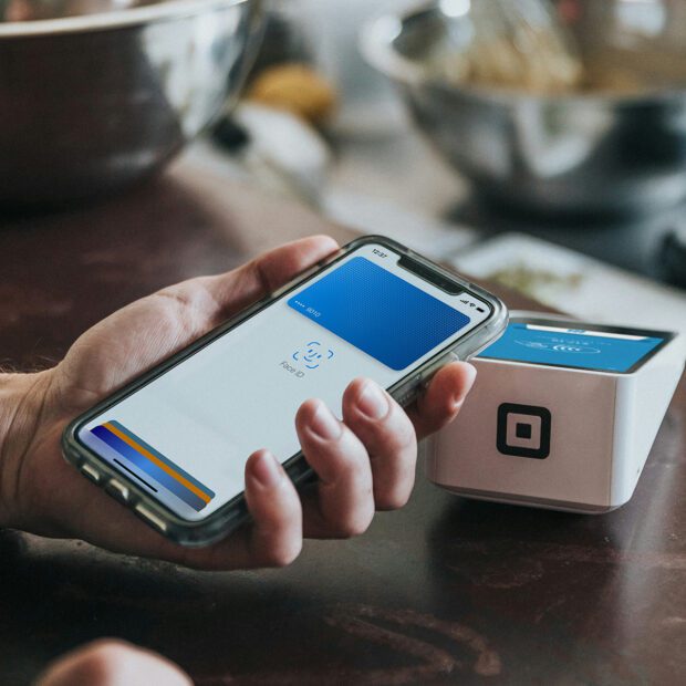 Frau hält iPhone mit Apple Pay an ein Zahlungsmodul