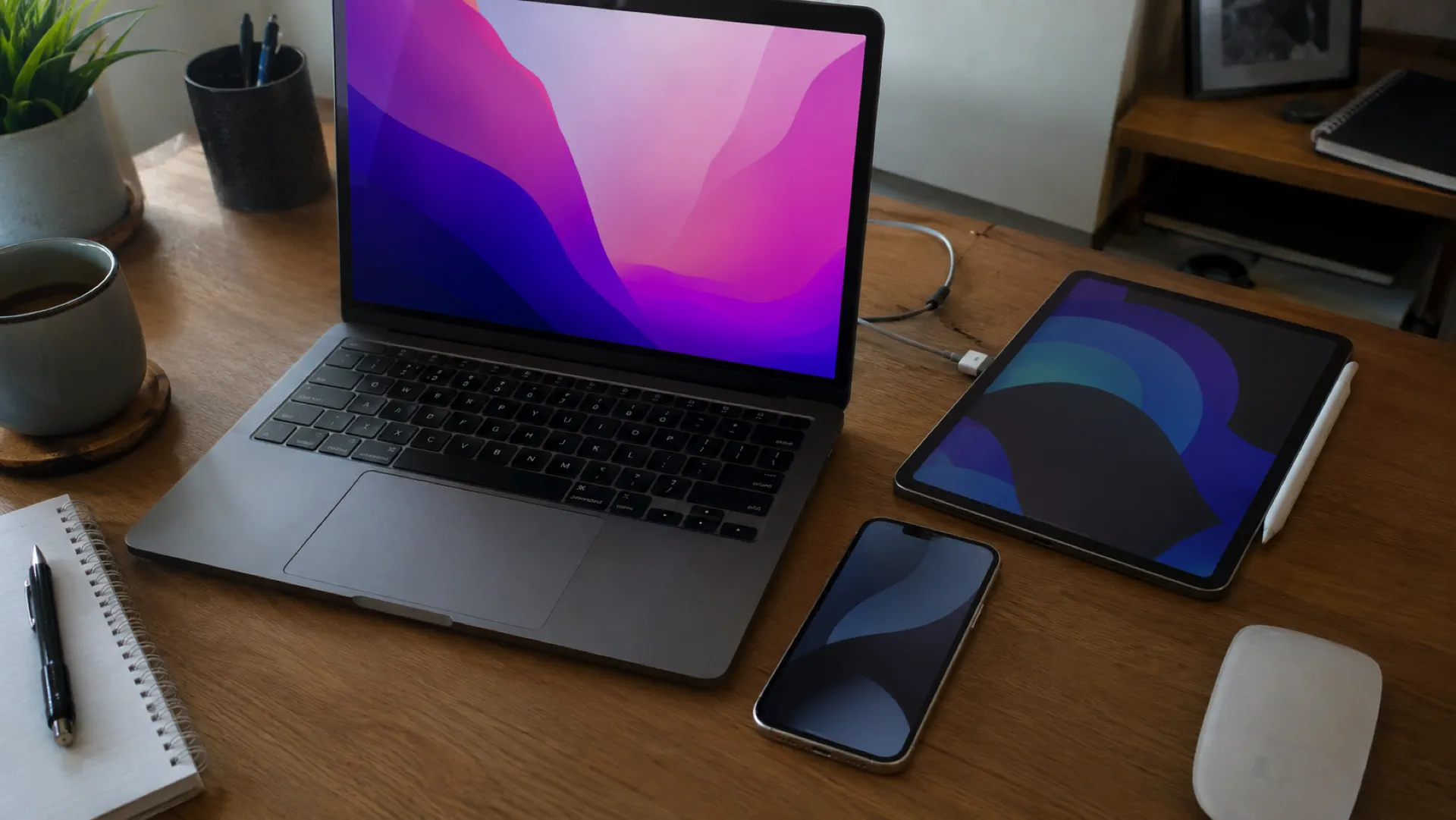 MacBook, iPad und iPhone nebeneinander auf einem Schreibtisch.